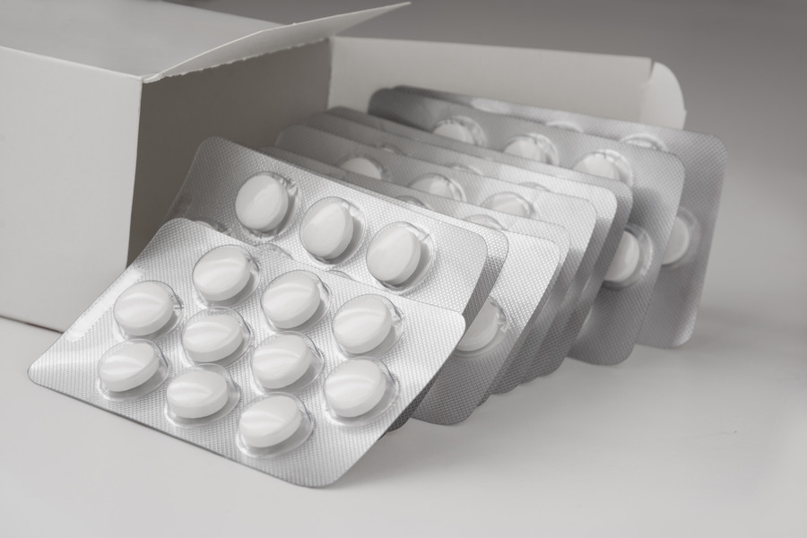 Closeup shot of white tablets inside of blister packaging besides a box