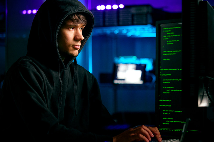 Low Key Lighting Shot Of Male Computer Hacker Sitting In Front Of Screens Breaching Cyber Security