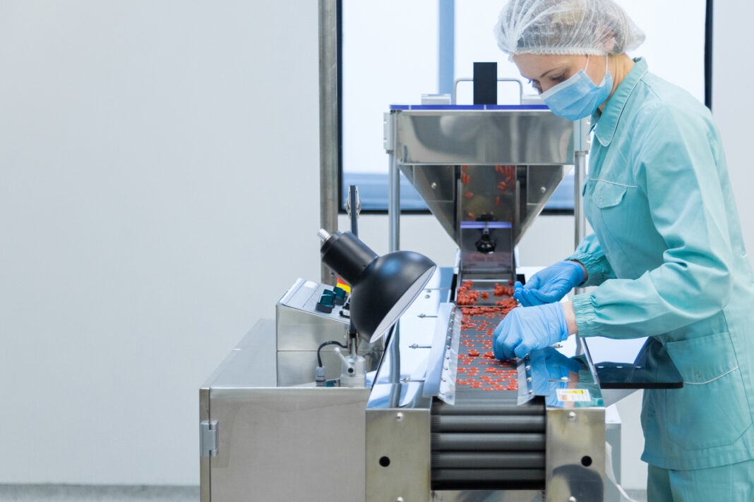Pharmacy industry woman worker in protective clothing operating production of tablets in sterile working conditions