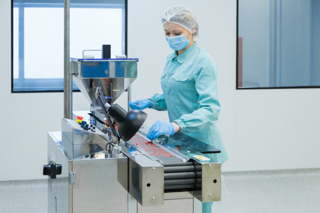 Pharmacy industry woman worker in protective clothing operating production of tablets in sterile working conditions Управление качеством ЛП