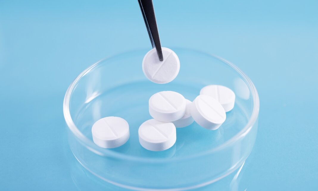 Closeup shot of tweezers picking up a white pill from a pile in a glass dish at a lab таблетки